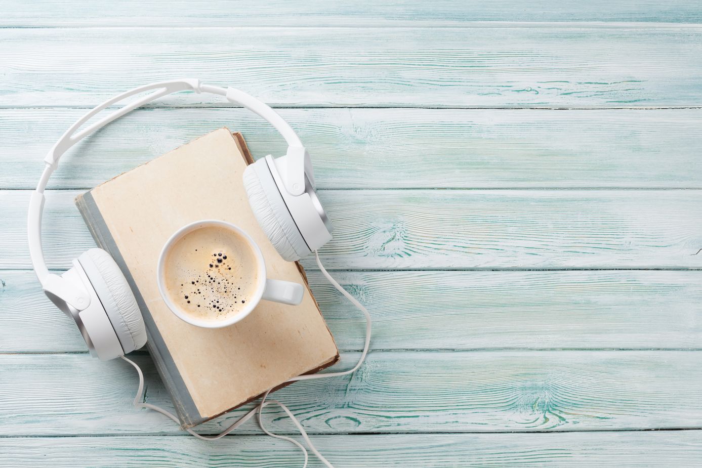 Audio book concept. Headphones, coffee and book over wooden table. Top view with space for your text