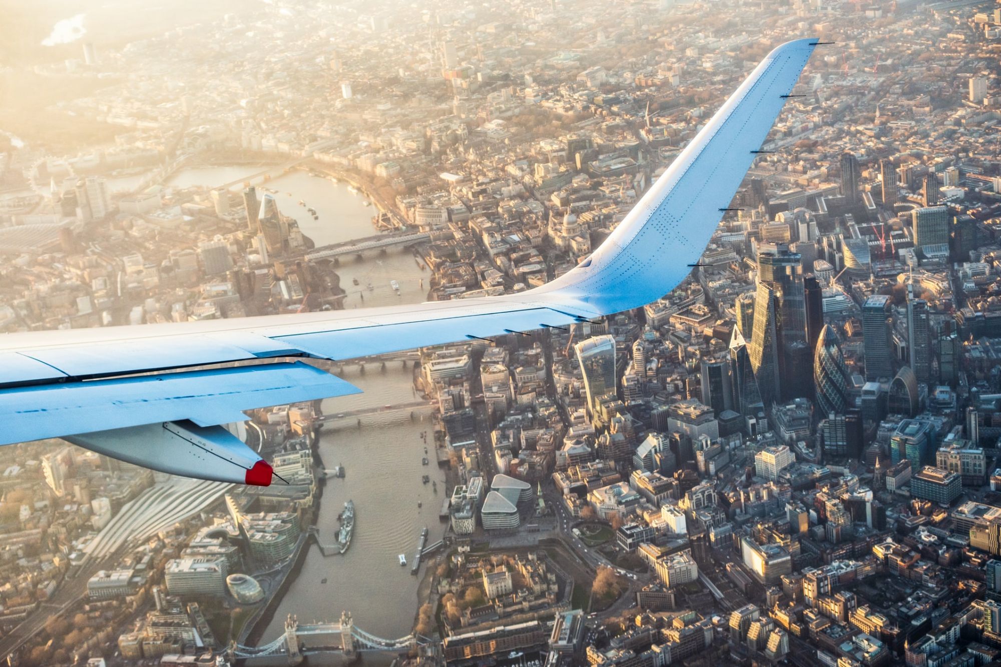 Wing of plane flying over London at golden hour