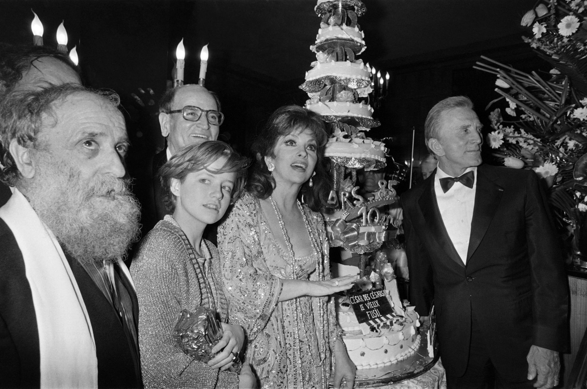 (from L), French sculptor Cesar, French actress Laure Marsac, Italian actress Gina Lollobrigida and US actor Kirk Douglas pose next to a cake to mark the 10th nuit des Cesar ceremony, on February 02, 1980, in Paris. Background, film producer Georges Cravenne. AFP PHOTO JEAN-LOUP GAUTREAU / PIERRE VERDY (Photo by - / AFP)