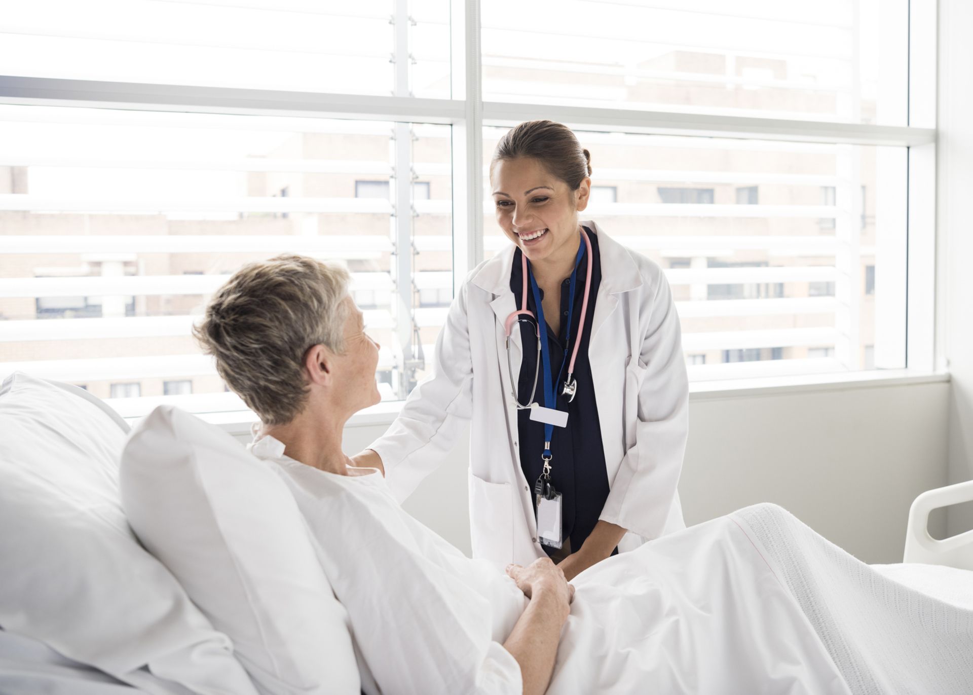 Senior woman in hospital bed listening to attractive female doctor. Medical professional caring for female patient in hospital bed.