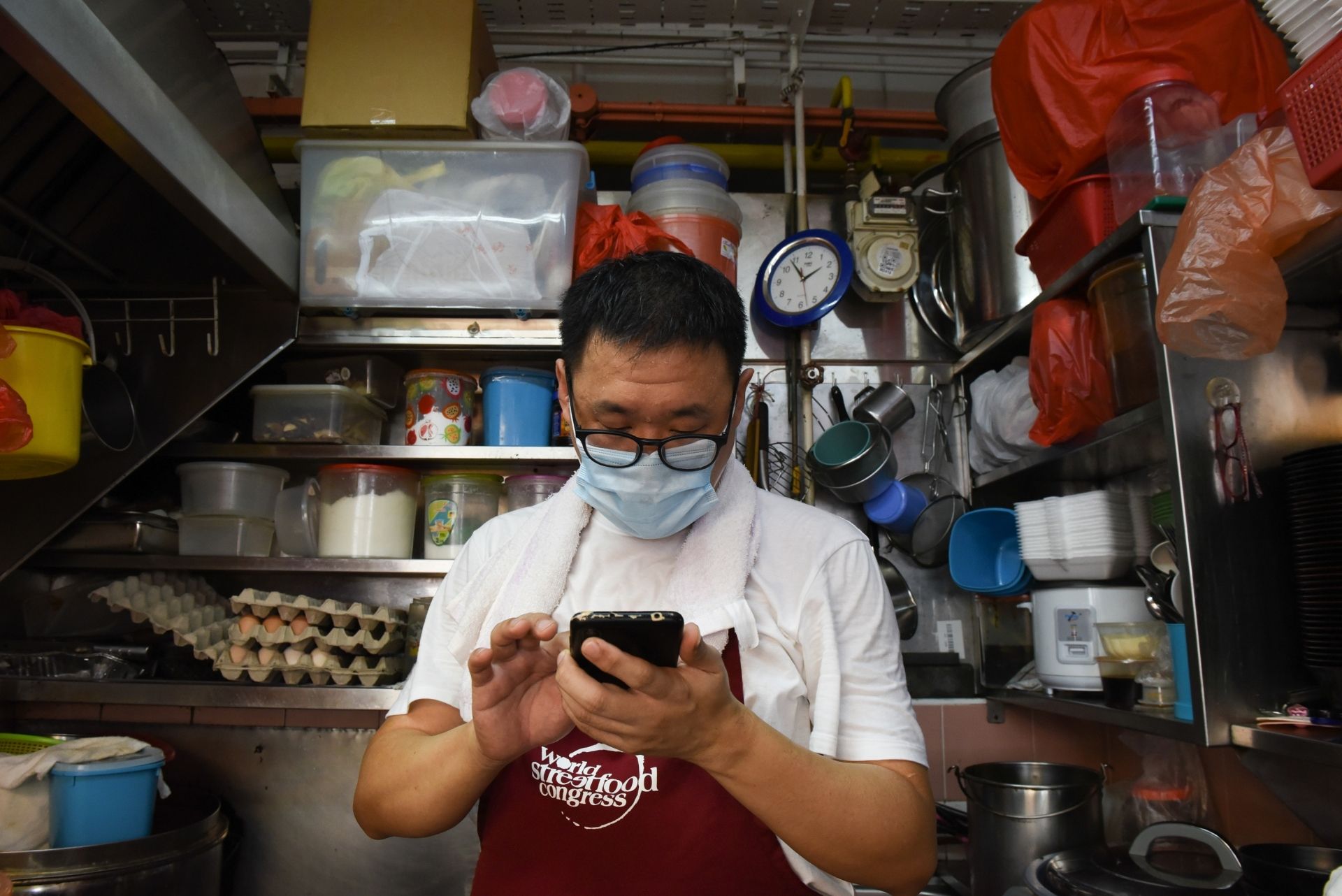 This photo taken on April 21, 2020 shows Melvin Chew scrolling through his phone at his small food stall, as the business has moved to delivery only due to the COVID-19 coronavirus outbreak in Singapore. - From Facebook groups to hyper-local delivery services, Southeast Asia's street food chefs are cooking up creative ways to sell their wares as they struggle to survive amid the coronavirus pandemic. (Photo by Catherine LAI / AFP)