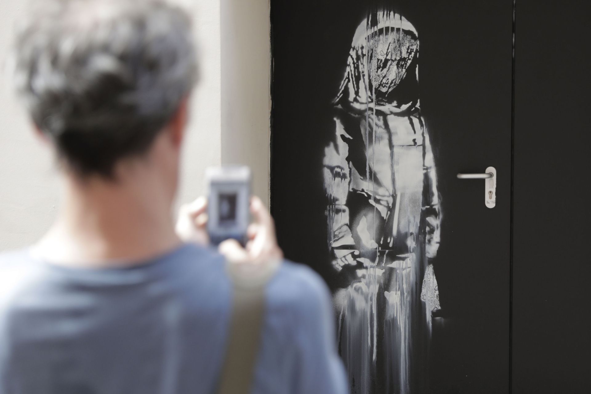 A man takes a photograph of a recent artwork by street artist Banksy in Paris on June 25, 2018, on a side street to the Bataclan concert hall where a terrorist attack killed 90 people on Novembre 13, 2015. - The mysterious British street artist has created a series of new murals in Paris in the last few days. (Photo by Thomas SAMSON / AFP)