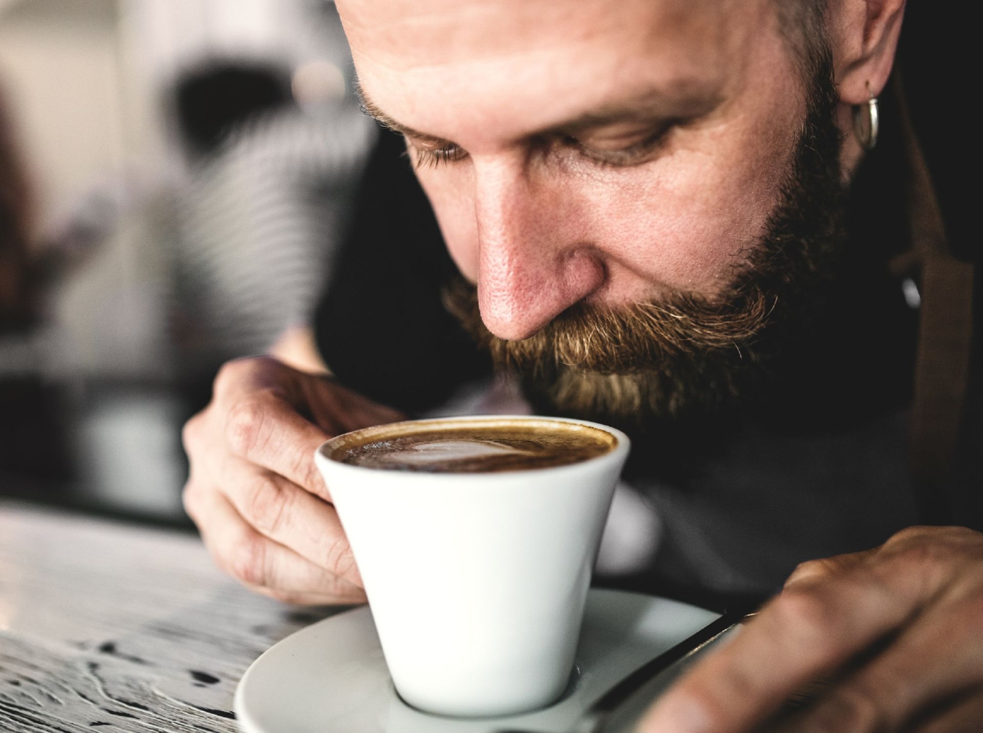 An mature man standing in a coffee shop, leaning over a cup of coffee.