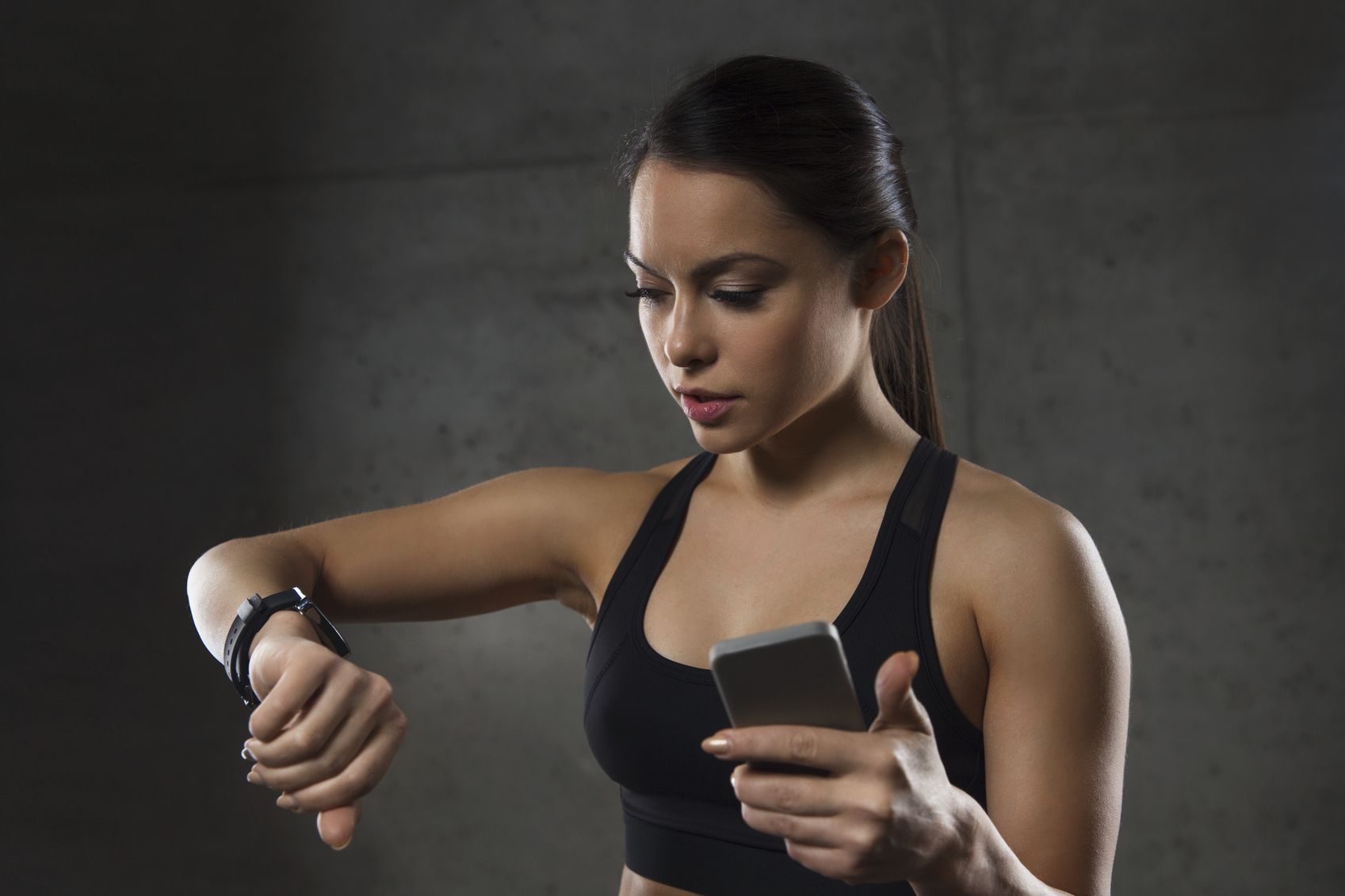 sport, fitness, technology and people concept - young woman with heart-rate watch and smartphone in gym