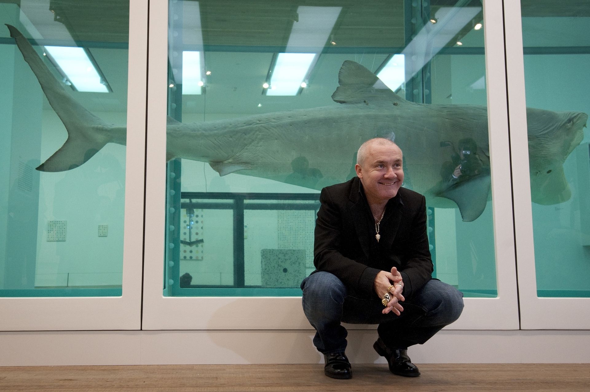British artist Damien Hirst poses for photographers next to his 1991 work 'The Physical Impossibility of Death in the Mind of Someone Living' during the opening of his solo exhibition showcasing work spanning over two decades at the Tate Modern in central London on April 2, 2012. AFP PHOTO / BEN STANSALL (Photo by BEN STANSALL / AFP)