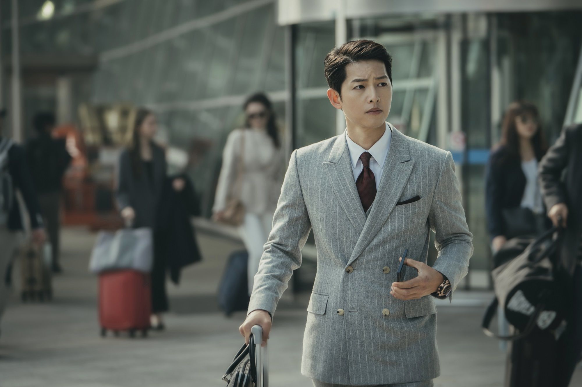 Vincenzo arrives in Korea in style with a grey, double-breasted coat paired with a dark brown tie - airport fashion never looked so good! | Photo: Vincenzo on Netflix