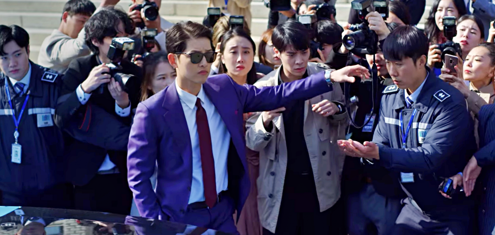Now, that's what you call an entrance. Vincenzo arrives at the courthouse in a blue suit, perfectly paired with a plum-coloured tie and sleek sunnies to match. | Photo: Vincenzo on Netflix