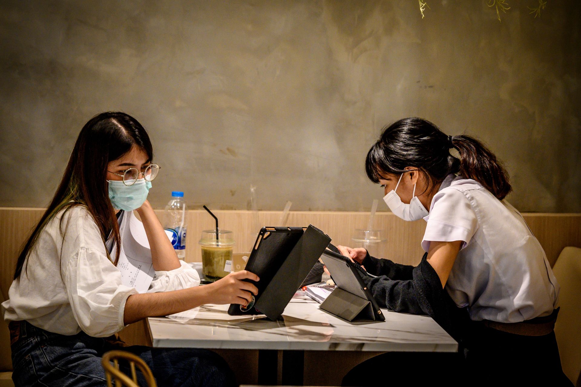 Students, wearing facemasks amid fears of the spread of the COVID-19 novel coronavirus, work in a coffee shop in Bangkok on March 3, 2020. - The world has entered uncharted territory in its battle against the deadly coronavirus, the UN health agency warned, as new infections dropped dramatically in China on March 3 but surged abroad with the US death toll rising to six. (Photo by Mladen ANTONOV / AFP)