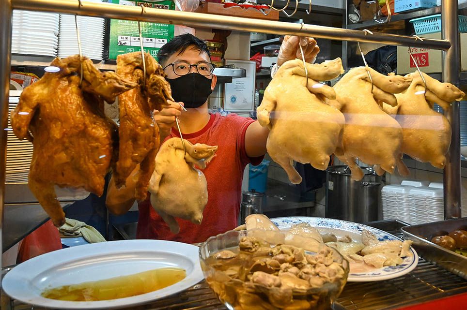 Hawker apprentice Lim Wei Keat displaying chickens at a chicken rice stall in Singapore. - Lim is among a small but growing number of young Singaporean street food vendors, or "hawkers", fuelling hopes that a new generation will preserve the city-state's culinary traditions. (Image: Roslan Rahman/AFP)