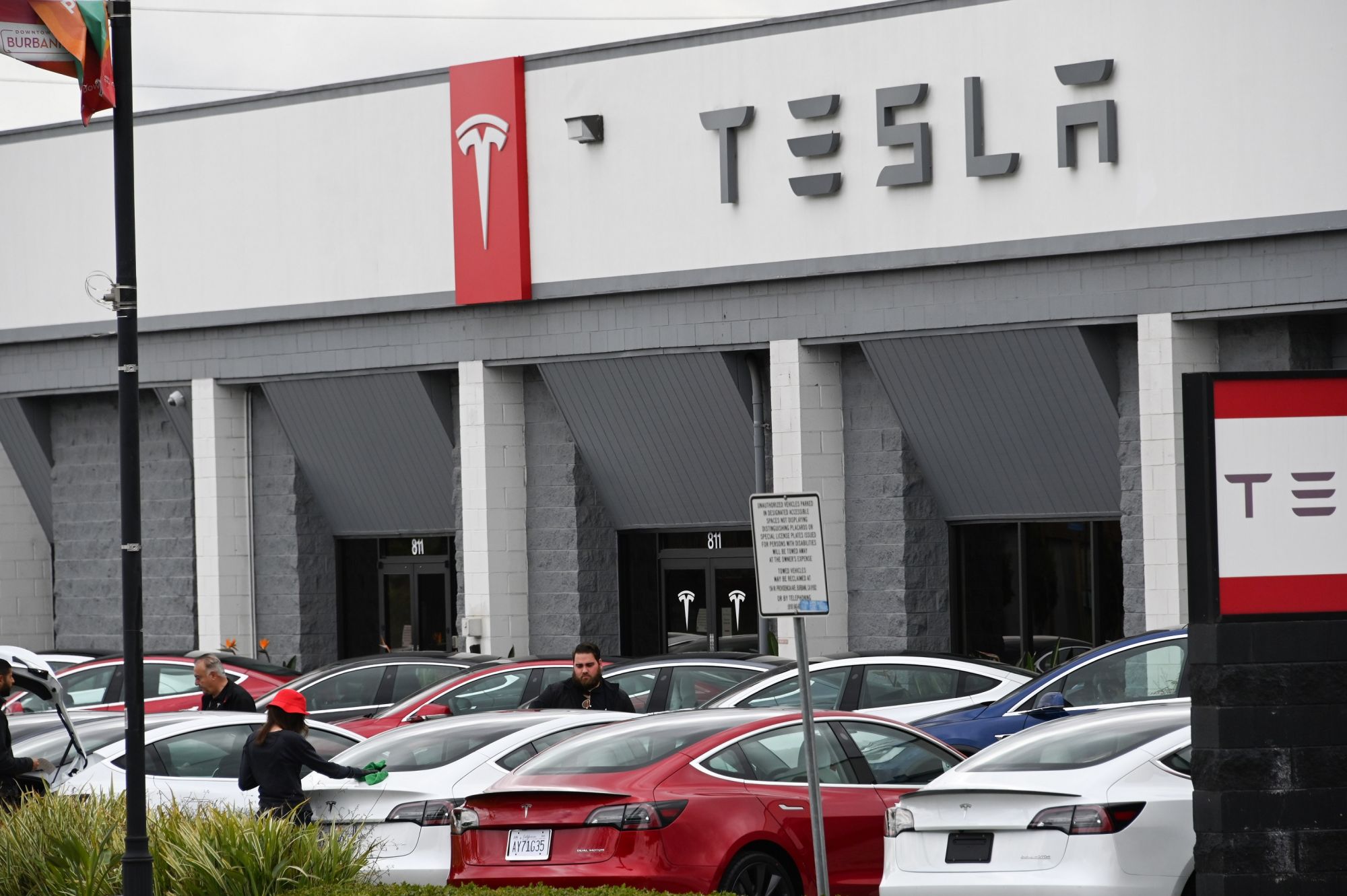 Telsa employees work outside a Tesla showroom in Burbank, California, March 24, 2020. - Luxury electric car maker Tesla ended up closing its California plant in Fremont, a concession by its maverick head Elon Musk after a drawn-out standoff with the state authorities over the spread of the virus. (Photo by Robyn Beck / AFP)