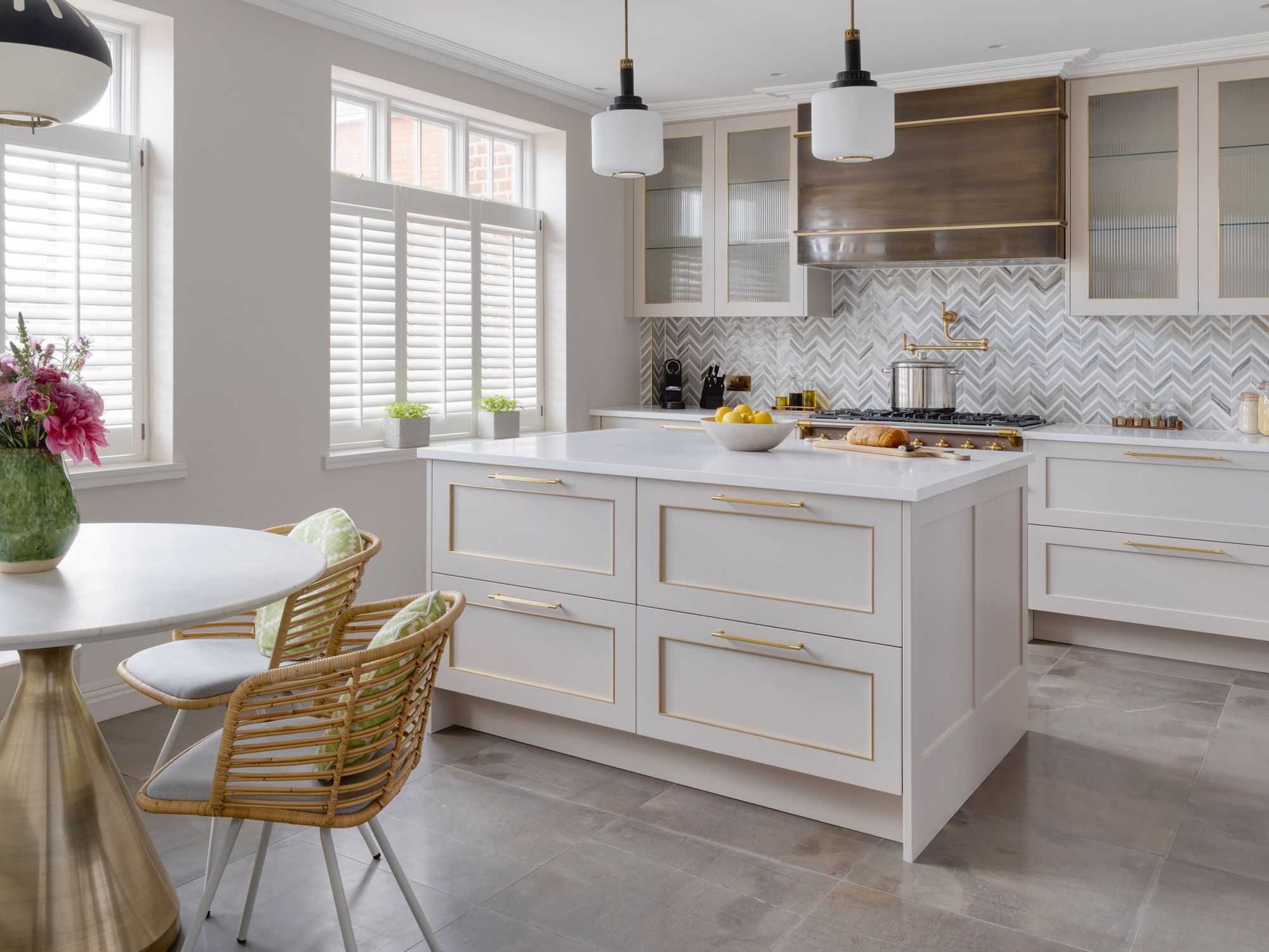 A herrigbone-patterned backsplash and Grigio Tunisi marble flooring contribute to the layered look of the kitchen’s neutral scheme