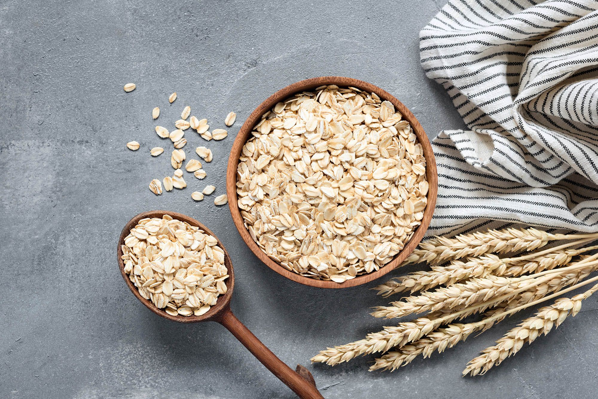 Oats, rolled oats or oat flakes in wooden bowl and wooden spoon. Top view. Healthy grains, low carb diet food