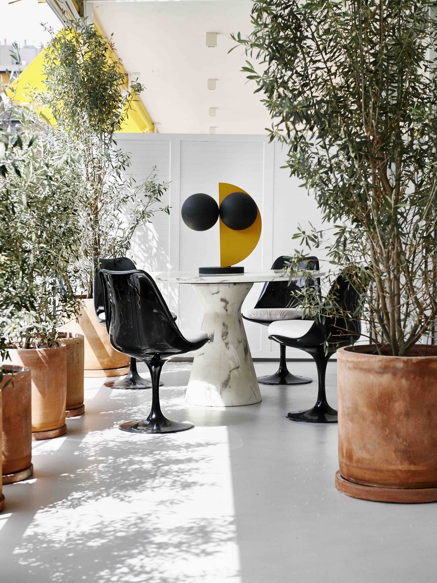 La salle à manger extérieure est meublée avec des chaises Knoll Tulip d'Eero Saarinen, une table de Recdi8 Living et une sculpture en bois de Rob Van Dam
