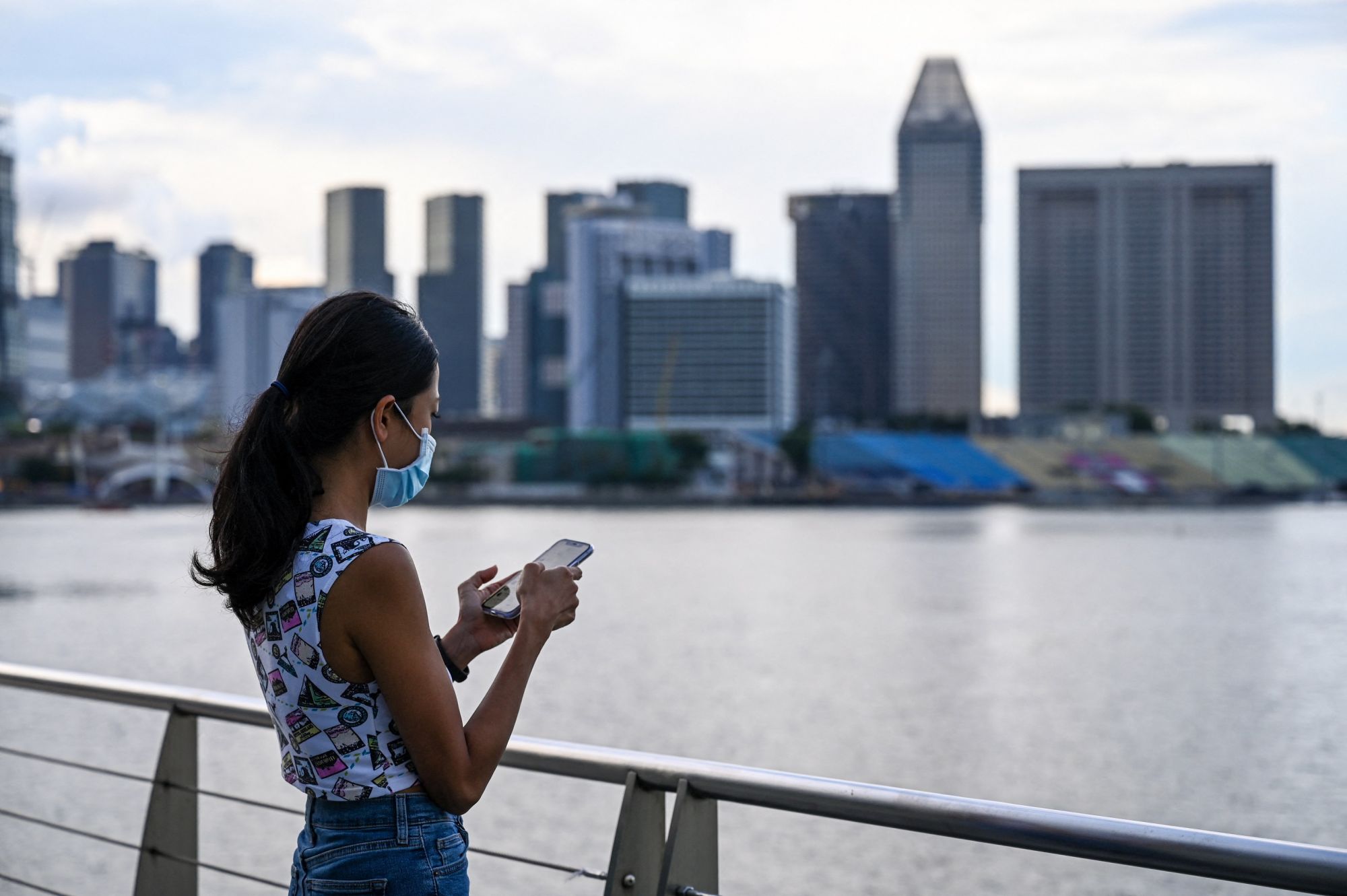This picture taken on May 7, 2021 shows an advertising executive who wanted to be known as Erica checking her mobile phone along the Marina Bay promenade in Singapore. - Erica is among a growing number of women travelling overseas to get their eggs frozen, as people in the work-obsessed city-state increasingly delay having children. (Photo by Roslan RAHMAN / AFP) / TO GO WITH Singapore-Malaysia-women-fertility, FEATURE by Catherine Lai and Sam Reeves