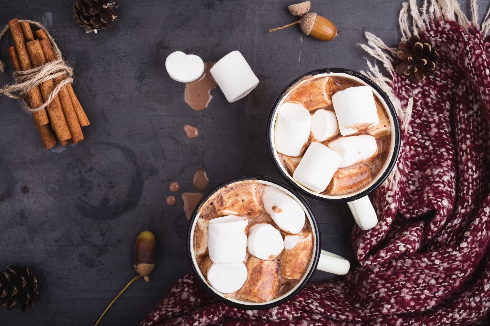 Hot chocolate served in vintage mugs with marshmallows for two person on table with woolen scarf wrapped around it, top view with copy space
