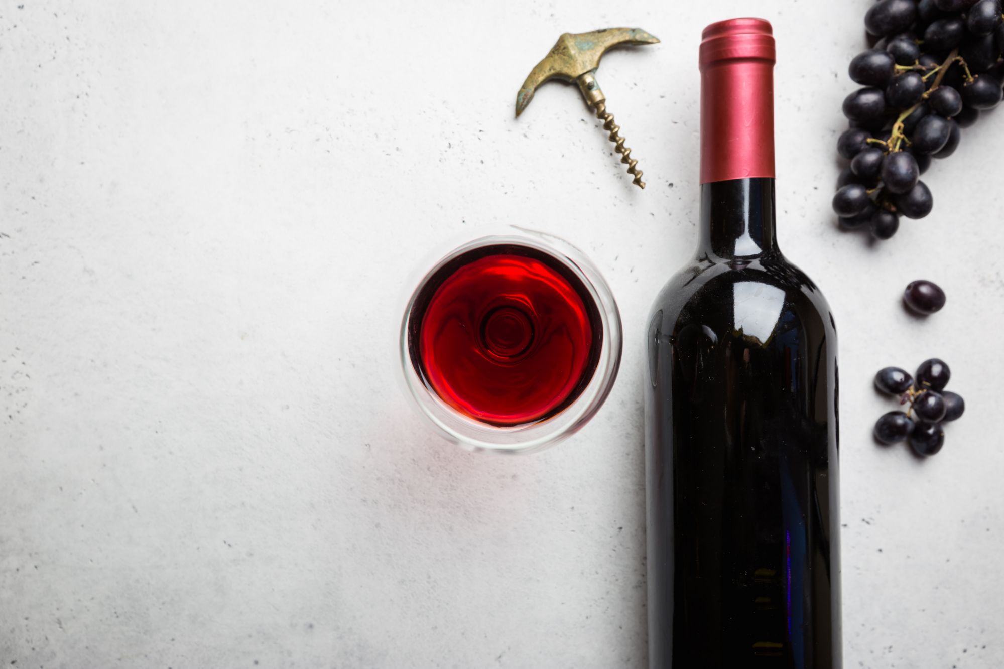 Red wine in a glass and ripe grapes on white background, top view