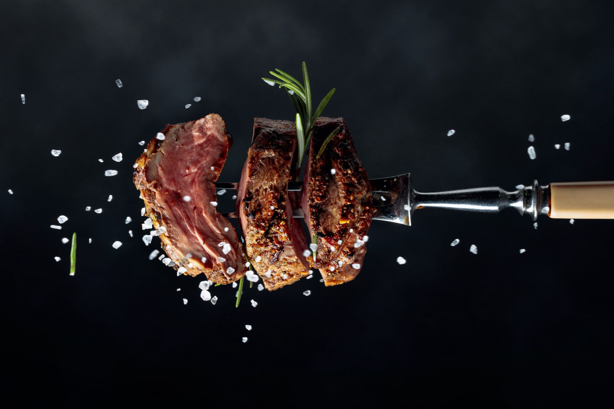 Grilled beef steak with spices on a black background. Beef steak on a fork sprinkled with rosemary and sea salt. (Grilled beef steak with spices on a black background. Beef steak on a fork sprinkled with rosemary and sea salt. , ASCII, 116 compon