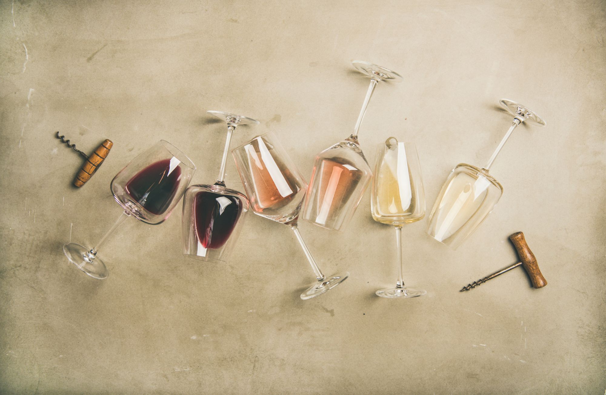 Flat-lay of red, rose and white wine in glasses and corkscrews over grey concrete background, top view, horizontal composition. Wine bar, winery, wine degustation concept