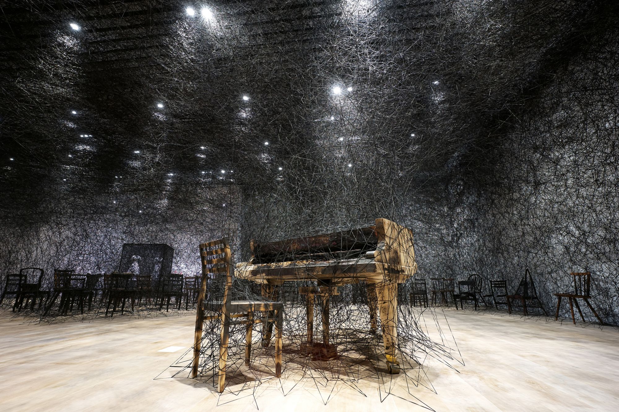 塩田千春,《寂靜中》(暫譯),2002/2019,燒焦鋼琴、燒焦椅、Alcantara黑線,尺寸視空間而定。製作贊助:Alcantara S.p.A 由Kenji Taki 畫廊,名古屋/東京提供 。展出現場:「塩田千春展:魂がふるえる」,東京森美術館,2019 攝影:Sunhi Mang 照片由森美術館提供