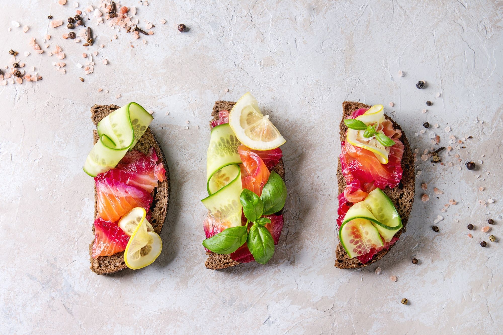 Sliced beetroot marinated salmon sandwiches with rye bread, cucumber, basil and lemon over grey texture background Top view, space. (Photo by: Natasha Breen/REDA&CO/Universal Images Group via Getty Images)