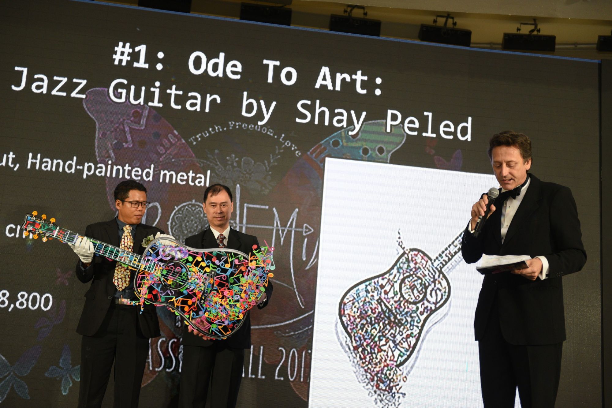 Auctioneer Andrew Thomas introducing the first item up for bid, a laser-cut metal guitar by artist Shay Peled