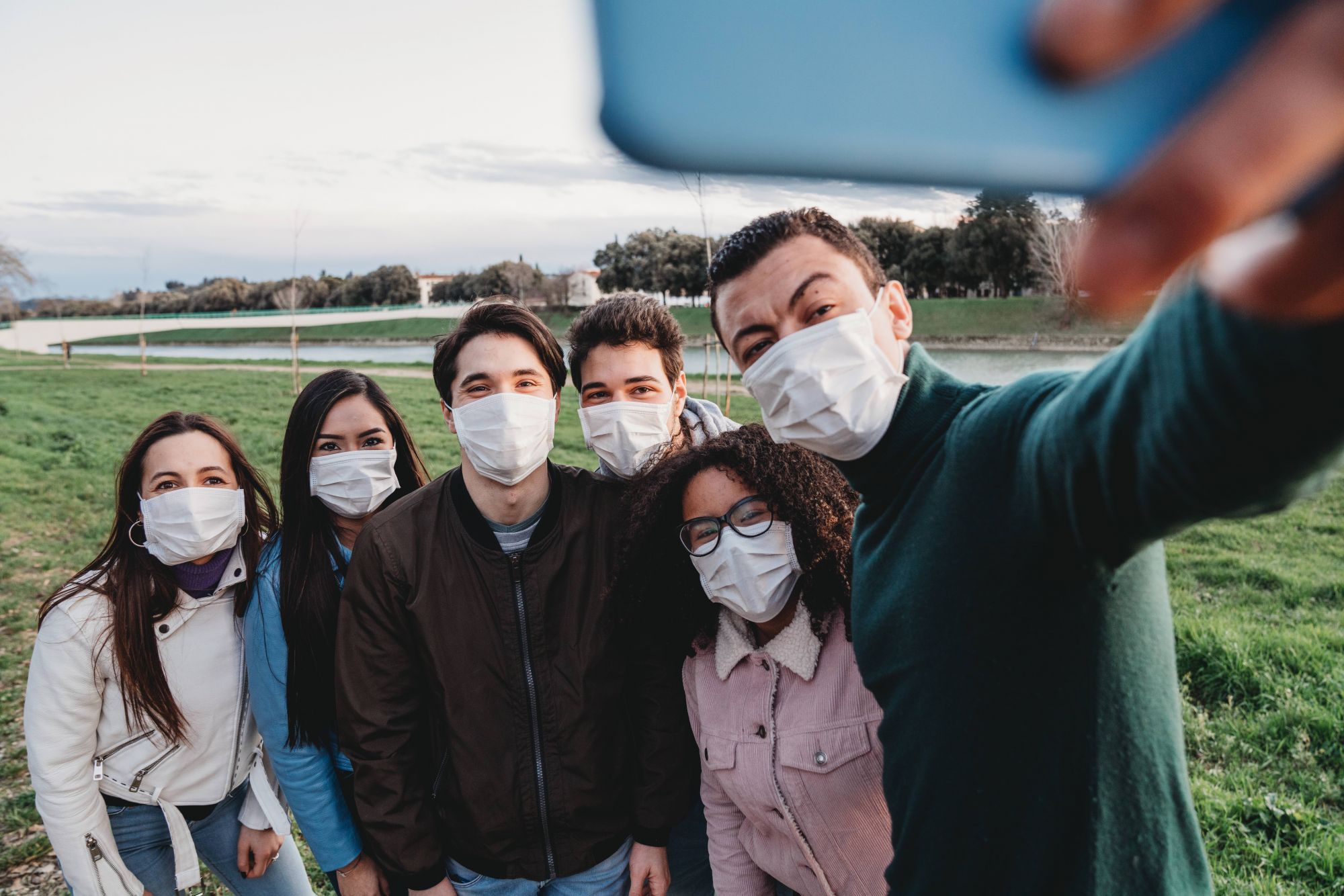 Group of six friends taking a selfie together while they are wearing protecting masks. Multi ethnic group of people wearing pollution masks to protect themselves from viruses.